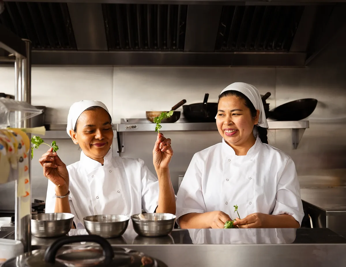 Two chefs sharing a laugh during prep in The Tiny Thai kitchen