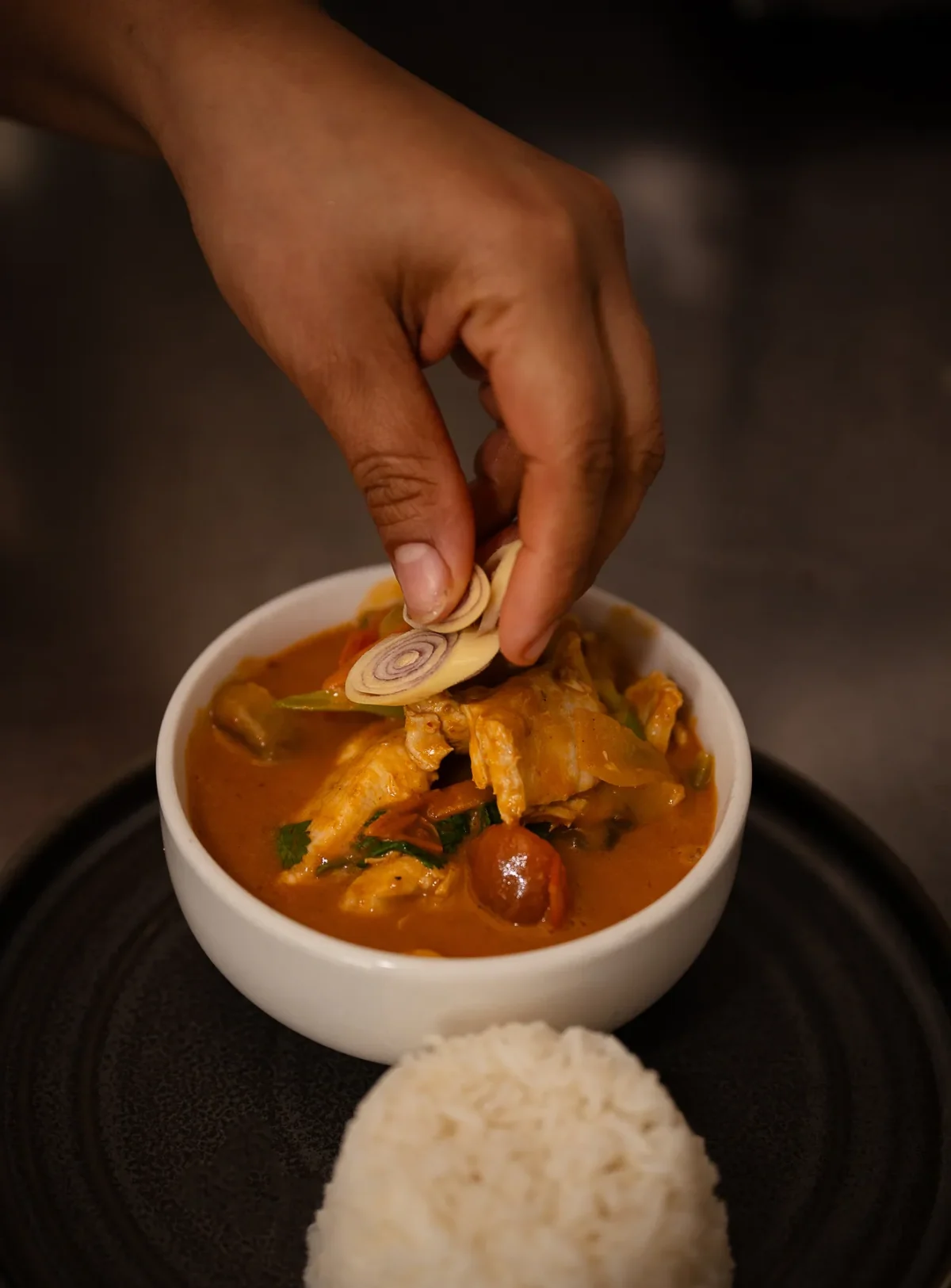 A chef's hand placing fresh basil on a bowl of rich Paneng curry beside jasmine rice