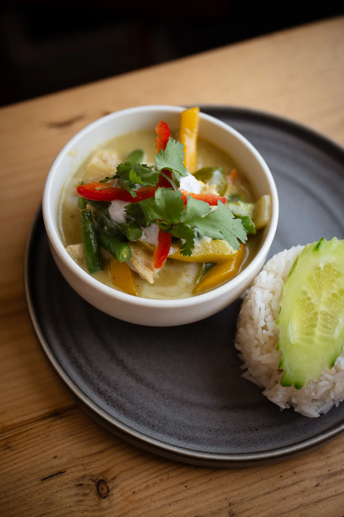 Green curry with chicken, peppers, green beans and coriander in a white bowl with jasmine rice