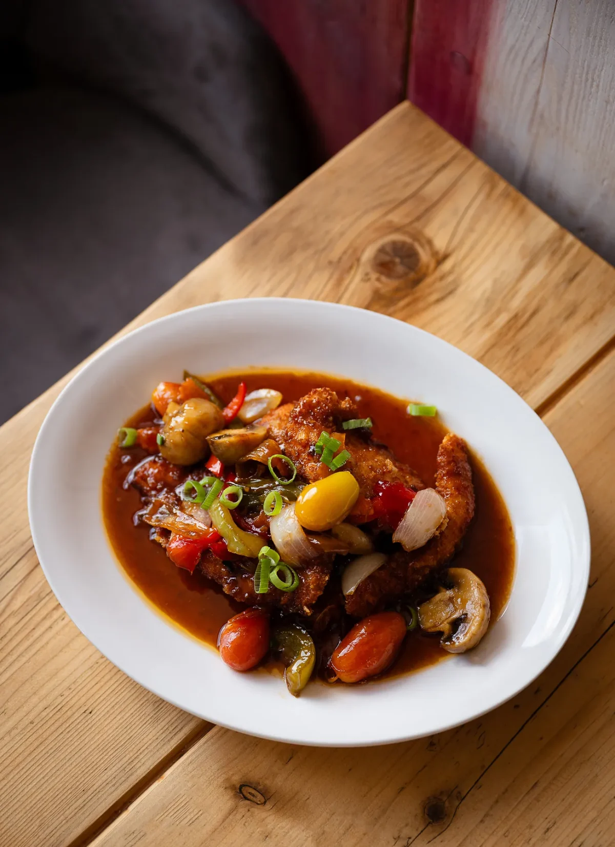 Sweet and sour chicken with peppers and tomato in a white bowl on a wooden table