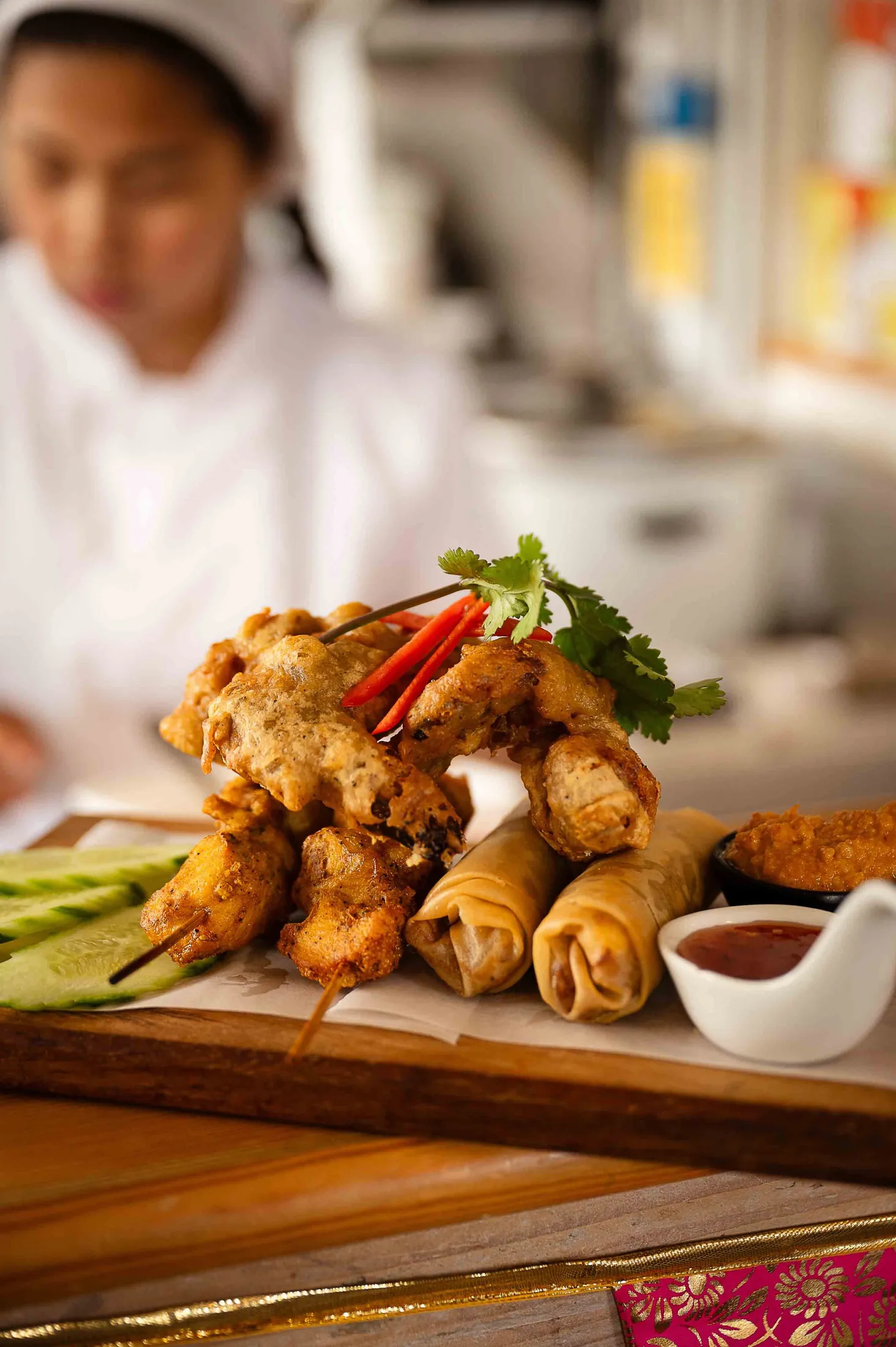 Crispy Thai starters on a board at the pass, with a chef working behind